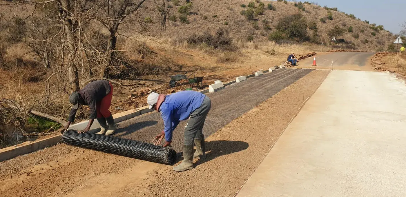 Workers unrolling reinforcement mesh across a prepared road surface